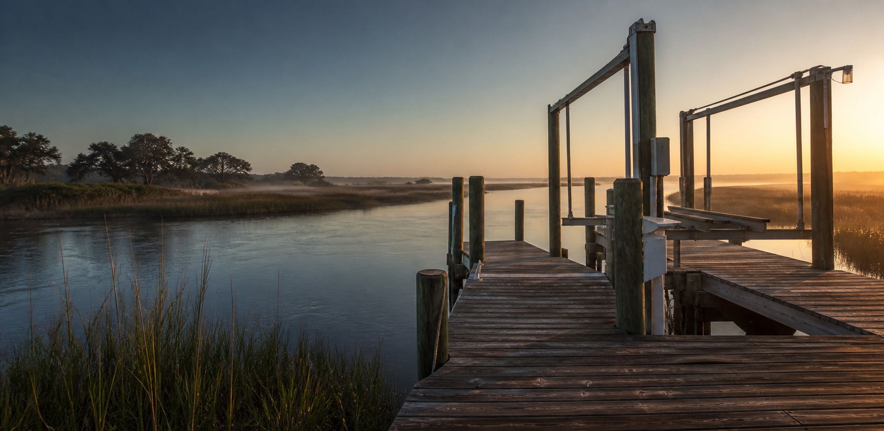 A wooden residential dock and boat lift overlooking a North Florida tidal marsh at sunrise